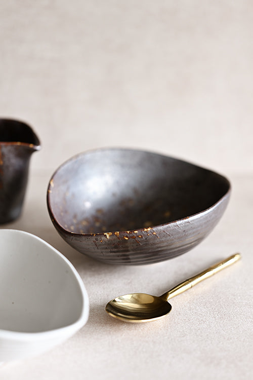 The Intimate Table pieces arranged on a neutral surface — Charcoal Grill Shell Dish, Gold Leaf Bowl, and Bamboo Polished Gold Serving Spoon