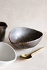 The Intimate Table pieces arranged on a neutral surface — Charcoal Grill Shell Dish, Gold Leaf Bowl, and Bamboo Polished Gold Serving Spoon