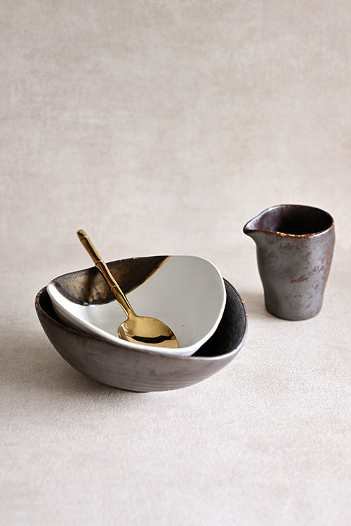 Gold Leaf Shell Bowl nested inside the Charcoal Grill Shell Sharing Dish, with the matching Pouring Jar and Bamboo gold serving spoon