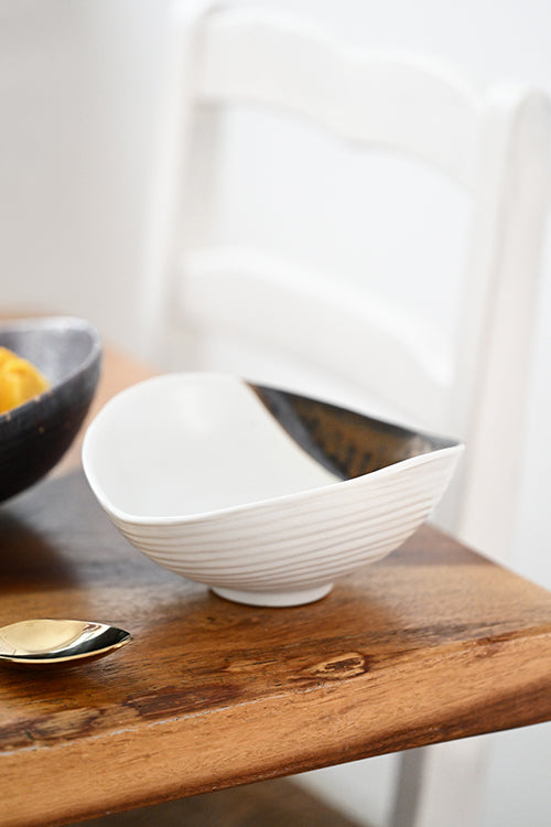 Close-up of the Gold Leaf Shell Presentation Bowl — matte white ceramic with hand-dipped bronze accent on a wood dining table
