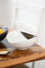 Close-up of the Gold Leaf Shell Presentation Bowl — matte white ceramic with hand-dipped bronze accent on a wood dining table
