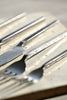 Macro detail of brushed stainless steel cutlery handles with squared minimalist profiles on a textured ceramic surface