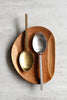 Square-handled brushed stainless steel and brushed gold serving spoons side by side on a wooden tray, top view
