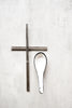 Top-down detail of square-handled stainless steel chopsticks crossed over a handmade ceramic soup spoon