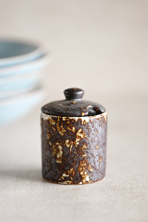 Dark ceramic jar holding sea salt on a wooden dining table